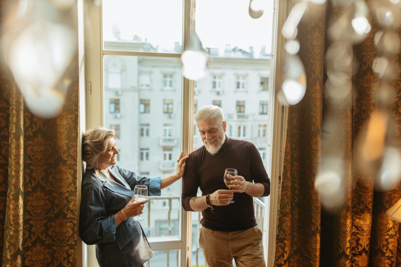 Un couple trinque en riant devant les hautes fenêtres de son appartement haussmannien