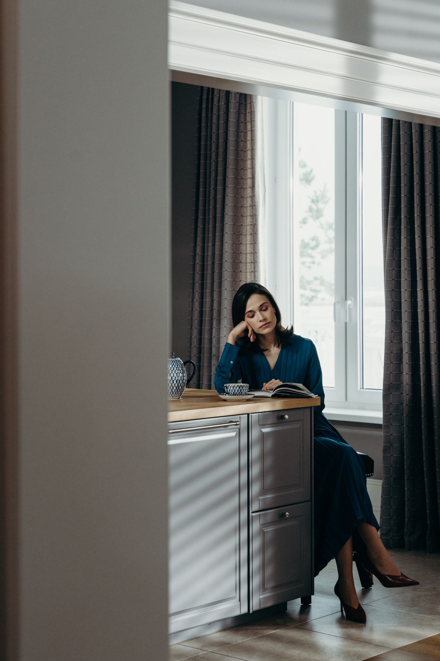 Une femme lit, installée près de la fenêtre de son appartement