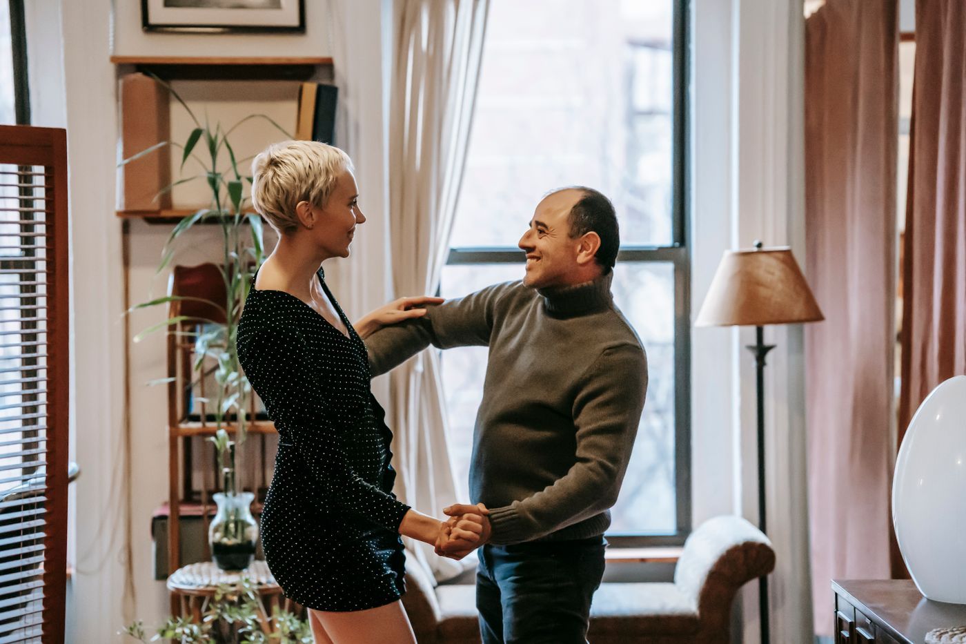 Un couple danse en riant devant les hautes fenêtres de son appartement